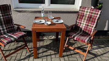 Een houten tafel met twee geruite stoelen, een fles en borden voor twee personen.