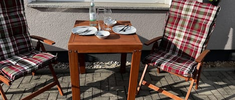 Ein Holztisch mit zwei karierten Stühlen, einer Flasche und zwei gedeckten Tellern.