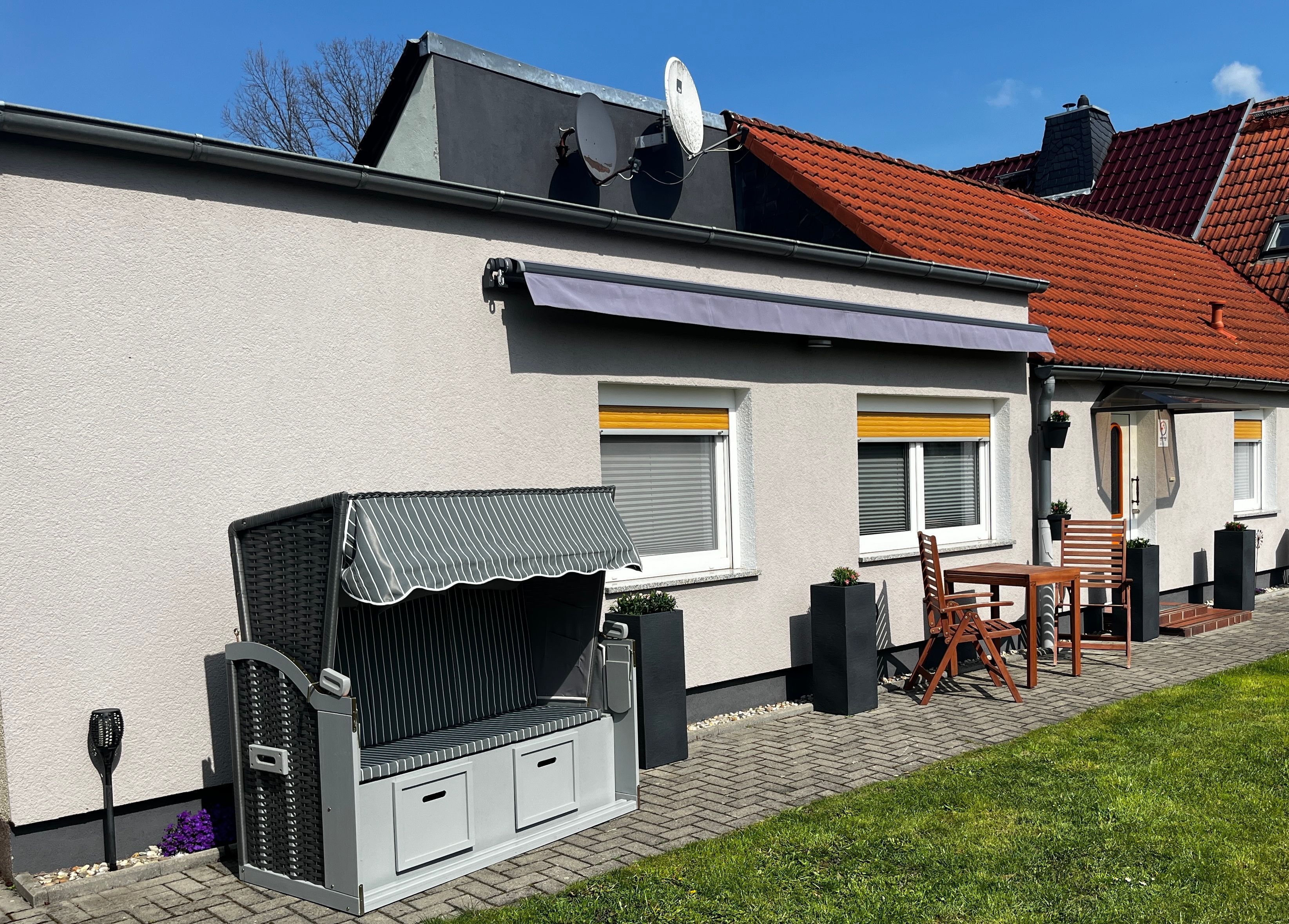 A house with a patio area featuring a grill, outdoor seating, and a small garden.
