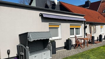 A house with a patio area featuring a grill, outdoor seating, and a small garden.