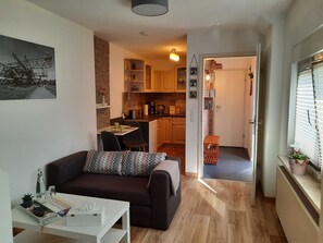 Um espaço compacto para viver, com um sofá, uma pequena mesa de jantar e um kitchenette.