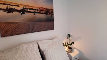 Una camera da letto con un letto, un comodino con una pianta e un quadro appeso al muro raffigurante un molo e l'acqua.