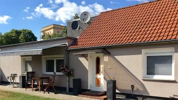 En tvåvåningsbyggnad med ett rött tegeltak, en satellantenn och en liten utesittplats med ett bord och några stolar.