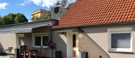 A two-story building with a red-tiled roof, a satellite dish, and a small outdoor seating area with a table and chairs.