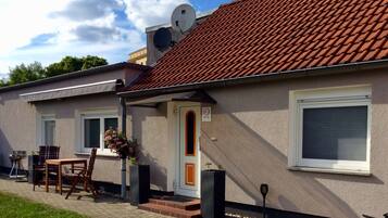 Ein Haus mit Ziegeldach, einer Haustür, einer kleinen Veranda mit Tisch und Stühlen sowie einer Satellitenschüssel.
