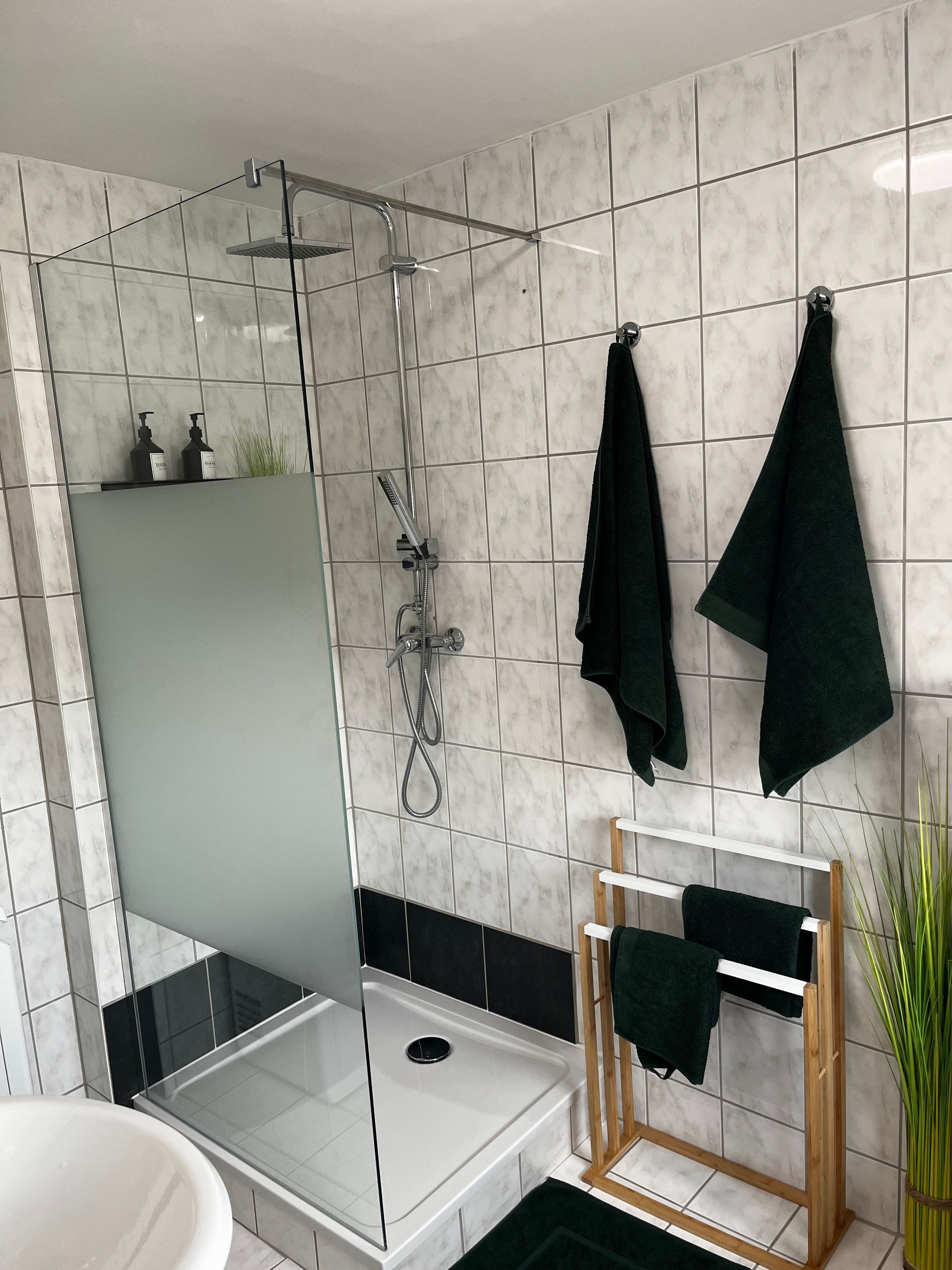 Ein modernes Badezimmer mit einer gläsernen Duschkabine, einer weißen Badewanne und einem hölzernen Handtuchhalter.