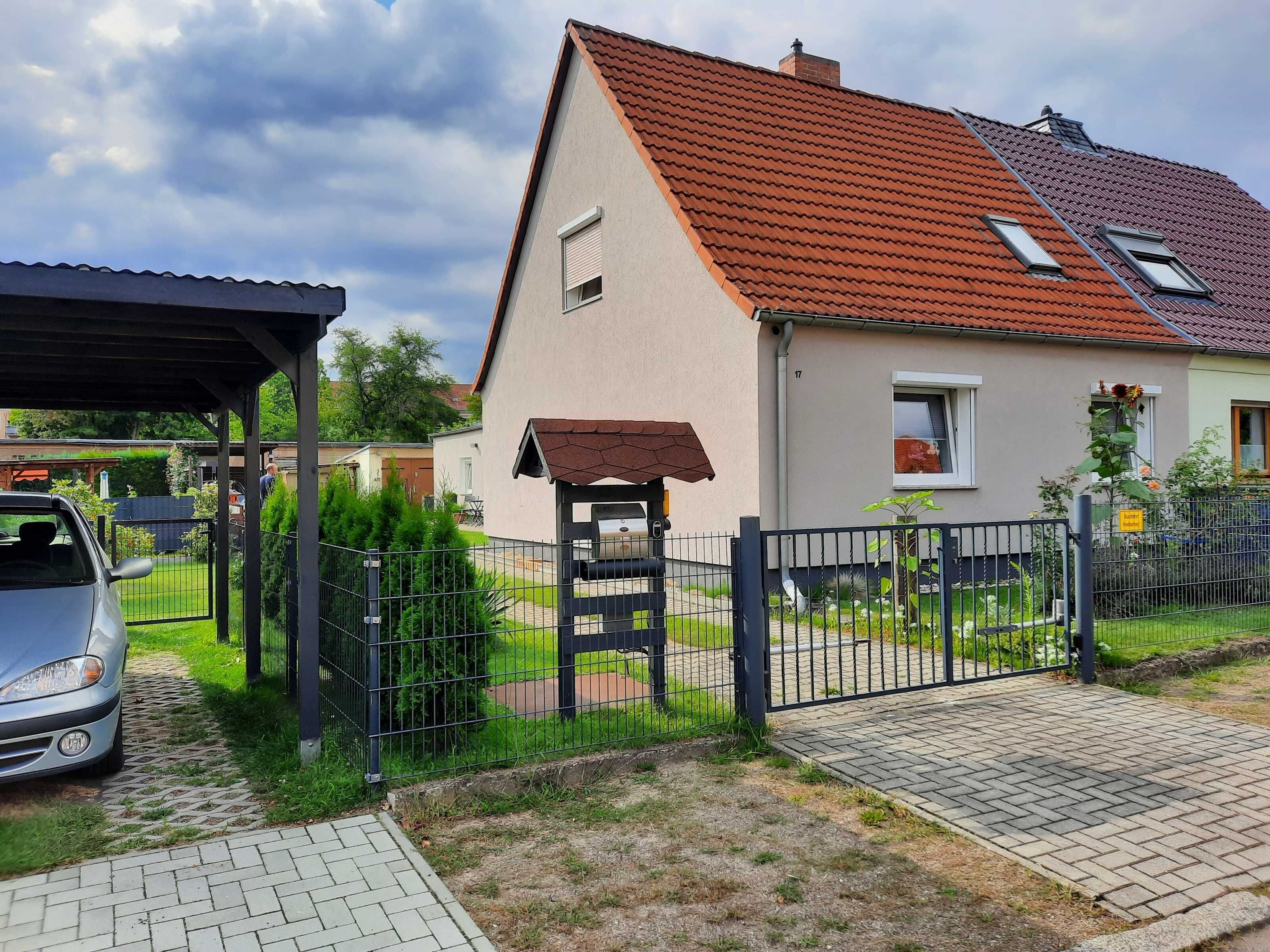 Ein Wohnhaus mit rotem Ziegeldach, einer Veranda und einem umzäunten Garten.
