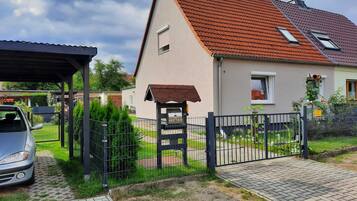 Ein Wohnhaus mit rotem Ziegeldach, einer Veranda und einem umzäunten Garten.