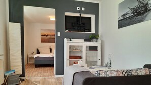 Ein modernes Wohnzimmer mit grauem Sofa, Holzboden, Wand-Fernseher und einer Vitrine.