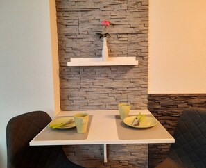 A dining area with a white table, two chairs, a vase with a single pink rose, and a yellow mug. - Vacation apartment Paula (Senftenberg)