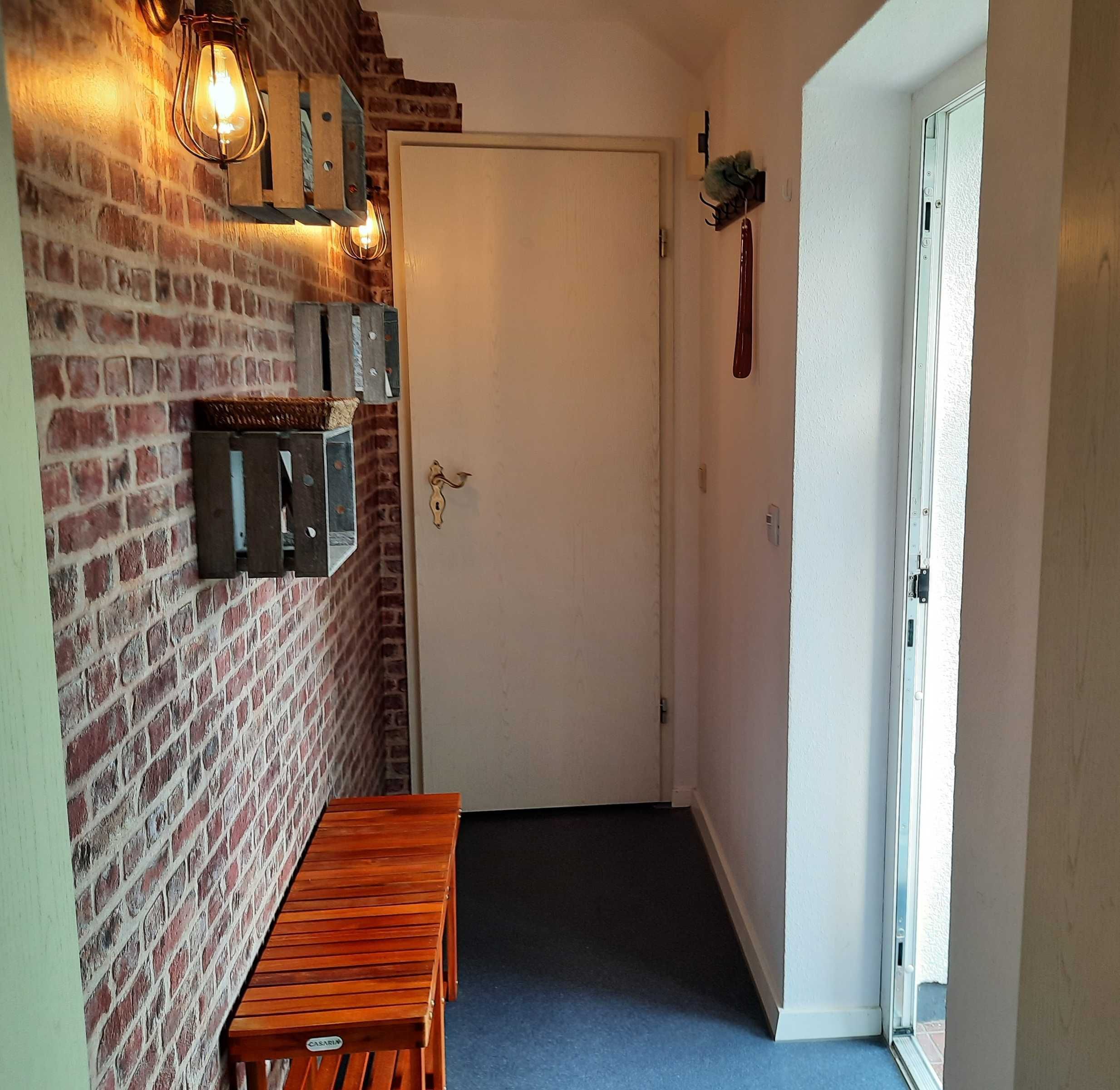 Ein Flur mit Backsteinwand, einer Holzbank, einer Tür und einer Wandleuchte.