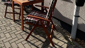 Eine Terrasse im Freien mit einem Holztisch und -stühlen, einem Grill und Blumentöpfen.