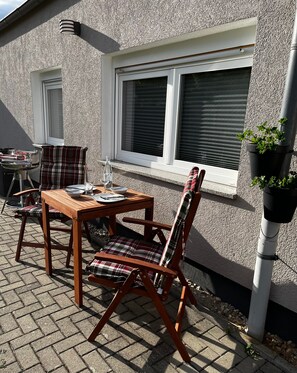 An outdoor patio with a wooden table and chairs, a grill, and potted plants. - Vacation apartment Paula (Senftenberg)