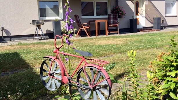 Ein rotes Fahrrad steht auf einer grünen Wiese, im Hintergrund ein Haus.