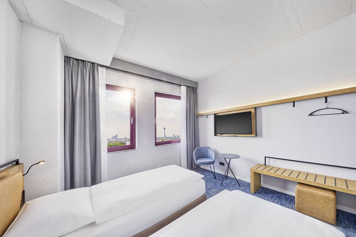 Une chambre d’hôtel avec deux lits, un bureau, une chaise, une télévision et une fenêtre avec des rideaux.