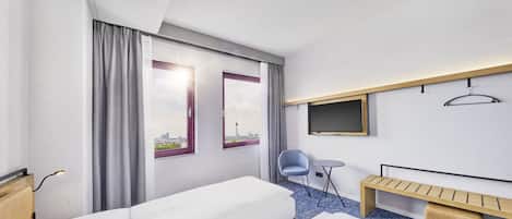 Una habitación de hotel con dos camas, un escritorio, una silla, un televisor y una ventana con cortinas.