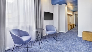 A hotel lobby with two chairs, a small table, a flat-screen TV, and a blue carpeted floor. - Sunday Hotel Düsseldorf Seestern (Düsseldorf)