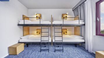 A room with bunk beds, two bedside tables with lamps, a window with curtains, and a blue carpet.