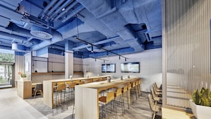 A modern office space with a long communal table, multiple chairs, and a large screen on the wall. - Sunday Hotel Düsseldorf Seestern (Düsseldorf)