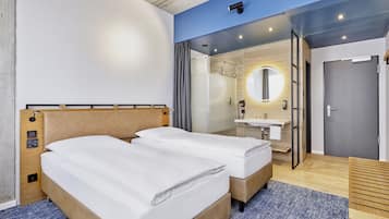 A modern hotel room with two beds, a bathroom with a mirror and sink, and a view of the city.