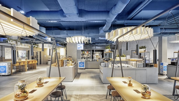 A modern restaurant with long wooden tables, hanging pendant lights, and a central island with a bar area. - Sunday Hotel Düsseldorf Seestern (Düsseldorf)