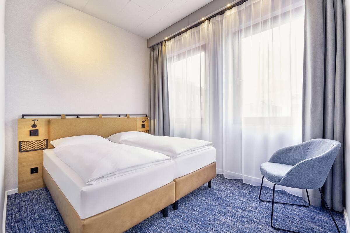Une chambre d’hôtel avec un lit, une chaise et une fenêtre avec des rideaux.