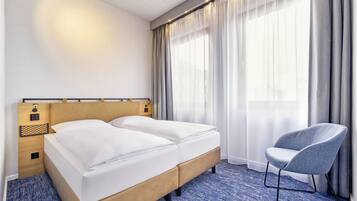 Una habitación de hotel con una cama, una silla y un ventanal con cortinas.