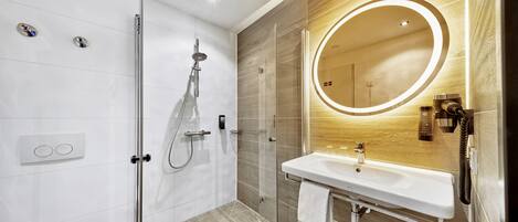 A modern bathroom with a glass-enclosed shower, a white sink with a wooden vanity, and a large mirror with a circular light.