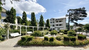 Een binnenplaats met een witte pergola, een bank en goed onderhouden hagen.