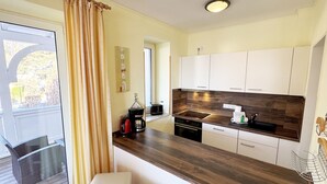 Een moderne keuken met een houten aanrecht, witte kasten en een ingebouwde oven. Op het aanrecht staan twee witte krukken en een koffiezetapparaat.