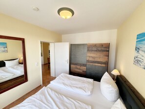 A hotel room with a bed, a large mirror, a painting, and a ceiling light. - MR: House Holstein Whg. 15 with balcony - House Holstein Whg. 15 with balcony (Sellin)
