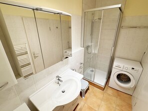 A modern bathroom with a sink, mirror, shower, and washing machine. - MR: House Holstein Whg. 15 with balcony - House Holstein Whg. 15 with balcony (Sellin)