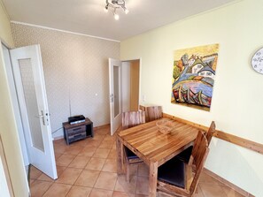 A dining area with a wooden table and chairs, a painting on the wall, and a clock. - MR: House Holstein Whg. 15 with balcony - House Holstein Whg. 15 with balcony (Sellin)