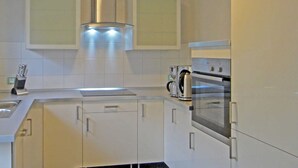 A modern kitchen with white cabinets, a stainless steel range hood, and a built-in oven.