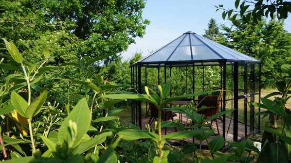 Un belvédère en verre doté d’une structure métallique, entouré d’une végétation luxuriante et d’arbres.