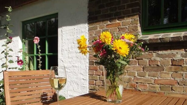 A wooden table with a glass of white wine and a vase of yellow flowers.