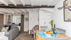 Una sala de estar acogedora con un sofá gris, una mesa de comedor de madera con mantel a cuadros y un jarrón de flores.