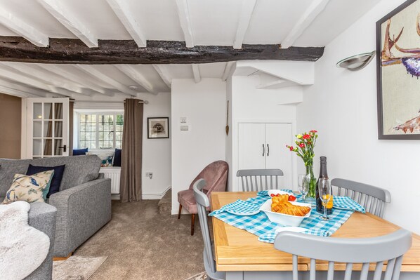 A cozy living room with a grey sofa, a wooden dining table with a checkered tablecloth, and a vase of flowers. - Church Cottage - a cotswold cottage that sleeps 4 guests in 2 bedrooms (Chipping Campden)