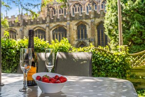 A table with a bottle of wine, two glasses, and a bowl of strawberries. - Church Cottage - a cotswold cottage that sleeps 4 guests in 2 bedrooms (Chipping Campden)