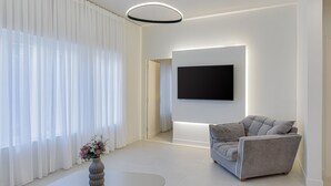 A modern living room with a flat-screen TV mounted on the wall, a grey sofa, and a vase with flowers on a white table. - Thiramenous Residence (Athens)