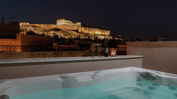 A rooftop terrace with a view of a historic building, a hot tub, and a table with wine and glasses. - Thiramenous Residence (Athens)