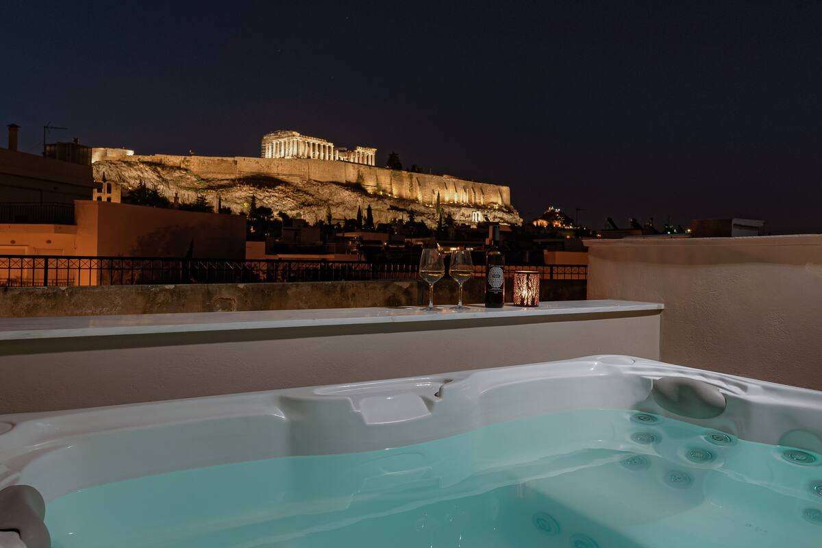 A rooftop terrace with a view of a historic building, a hot tub, and a table with wine and glasses.