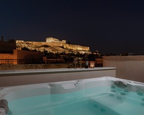 Terraza en la azotea con vistas a un edificio histórico, un jacuzzi y una mesa con vino y copas.