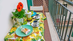 A balcony with a table set for two, featuring a floral tablecloth, a green chair, a vase with a single flower, and a green plate with food. - Large flat between two parks in central Florence-ideal for families/small groups (Firenze)