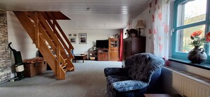 Uma sala de estar com escada de madeira, uma poltrona confortável, uma televisão e um armário com portas de vidro.