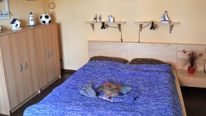 A bedroom with a bed, a wardrobe, two wall-mounted shelves with decorative items, and a hammock. - Apartment - Apartment Neuendorf (Saal)