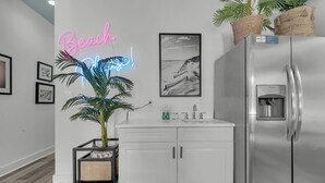 A kitchen with a stainless steel refrigerator, white cabinets, a sink, and a neon sign that reads "Beach, Now!" - Sea It All - 2303626 (Santa Rosa Beach)
