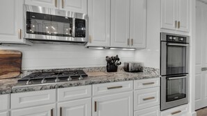 A modern kitchen with white cabinetry, stainless steel appliances, and a marble countertop. - Sea It All - 2303626 (Santa Rosa Beach)