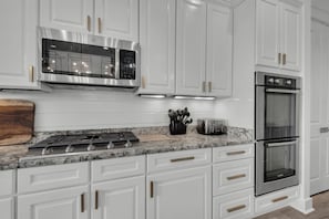 A modern kitchen with white cabinetry, stainless steel appliances, and a marble countertop. - Sea It All - 2303626 (Santa Rosa Beach)