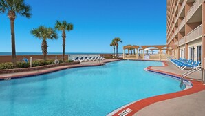 A swimming pool with blue water, surrounded by lounge chairs and palm trees, with a building in the background. - Sunrise Resort by BBG (Panama City Beach)